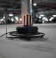 A coiled black heavy-duty cable on a metal dispenser stand sitting on the floor of a dimly lit underground parking garage.